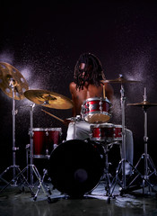 Fototapeta na wymiar wet drum set covered with water drops, african young man beating on drum set with sticks. skillful black drummer with naked skin and dreadlocks