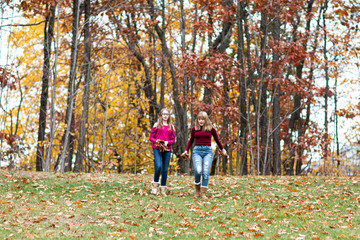 Fototapeta premium two young beautiful happy teenager girls, sisters and friends playing, running, jumping in forest. Colorful Fall, Autumn