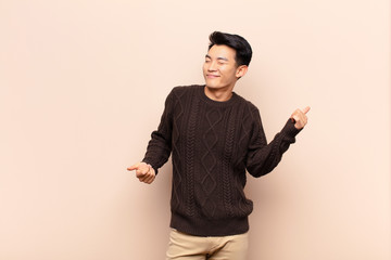 young chinese man smiling, feeling carefree, relaxed and happy, dancing and listening to music, having fun at a party against flat color wall