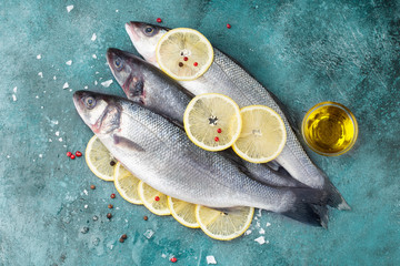 Fresh sea bass fish and lemon cut into rings, olive oil, salt, pepper on turquoise grunge background. Top view
