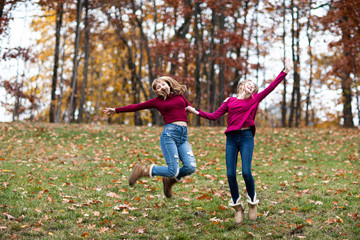 two young beautiful happy teenager girls, sisters and friends playing, running, jumping in forest. Colorful Fall, Autumn