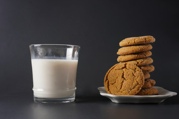 A glass of cold milk next to a stack of gingerbread cookies on a white plate with a black background