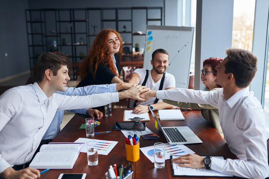 Solving problems as one team. Caucasian young team of male and female working together while sitting at their working place in office, enjoy