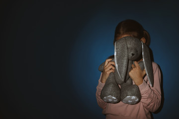 Little girl with toy near blue wall, space for text. Domestic violence concept