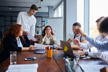 Young business people sad with result of their work, disappointed redhaired woman sit in the center of table