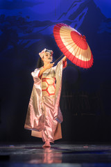 Traditional Japanese performance. Actress in traditional kimono and fox mark dancing with umbrella.