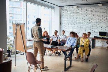 Ambitious young caucasian coach leader give presentation to co-workers sitting listening to him in...