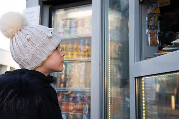 A child in winter clothes attentively examines the window of a street kiosk.