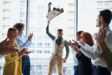 Young business leaders celebrate win of their arabian colleague standing in the center in pose of...