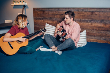 boyfriend and girlfriend playing the guitar, young caucasian couple in love with each other in bedroom.