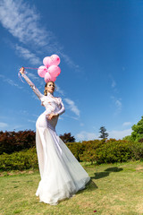 girl in a white long dress with pink balloons on the nature