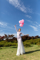 girl in a white long dress with pink balloons on the nature