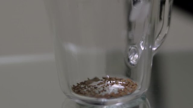 Instant coffee is poured into clear glass on table, close-up