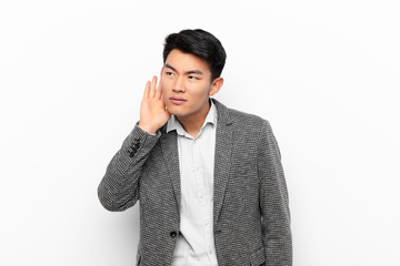 young chinese man looking serious and curious, listening, trying to hear a secret conversation or...