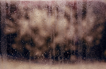 Wet window. Water raindrops on window glass with autumn or winter background. Depression, melancholic seasonal mood. Texture, abstract background. Weather concept