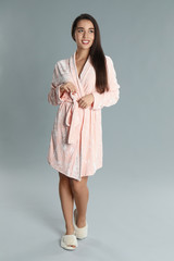 Beautiful young woman in bathrobe on grey background