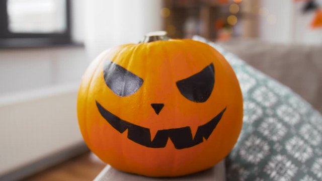 holidays, decoration and party concept - jack-o-lantern pumpkin with scary smiley on sofa at home on halloween