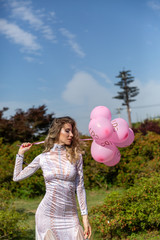 girl in a white long dress with pink balloons on the nature