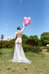 girl in a white long dress with pink balloons on the nature