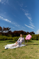 girl in a white long dress with pink balloons on the nature