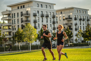 Two young attractive athletes run in the park of a modern city