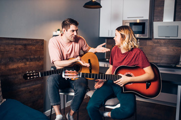 caucasian couple talking with each other during playing guitar, wearing casual wear