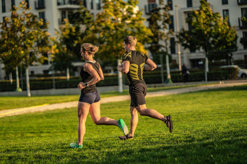 Two young attractive athletes run in the park of a modern city