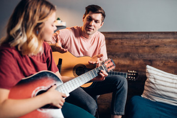 Obraz premium two romantic people in love sit together on bed, playing the guitar. caucasian people sit together at home