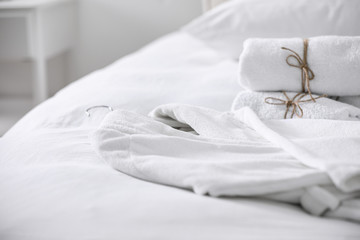 Clean soft bathrobe and towels on bed - obrazy, fototapety, plakaty