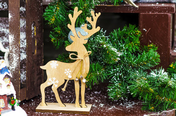 wooden figurine of deer on brown background next to fir branches, snow, snowflakes, garlands. Traditional home decor and symbol for Christmas and New Year holidays.