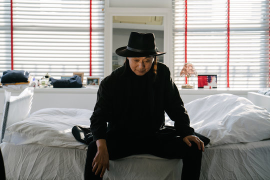 ベッドに腰掛ける、帽子を被ったシニア男性のポートレート