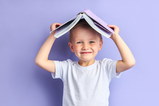 Portrait of joyful caucasian child in casual clothes after education, after reading wants to play. Funny boy holding book above his head, looking at camera - Powered by Adobe