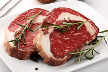 Raw fresh meat Ribeye Steak, seasoning and meat fork on rustic background