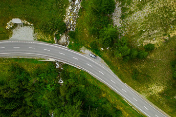 Aerial view from drone on a gray car on the side of the road. There is flowing mountain river in the forest in Switzerland.