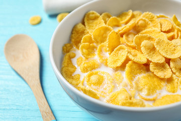 Tasty crispy corn flakes with milk on light blue table, closeup