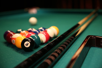 Sports game of billiards on a green cloth. Multi-colored billiard balls in the form of a triangle with numbers, two cues, a cue ball and a triangle on a pool table. Billiards billiard balls close up.