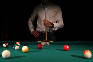 Sports game of billiards on a green cloth. Male player with a cue in his hands. Billiard balls with...