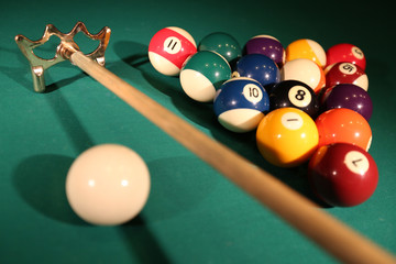 Sports game of billiards on a green cloth. Multi-colored billiard balls in the shape of a triangle with numbers,  cue and a triangle on a pool table. Billiards and billiard balls close up.