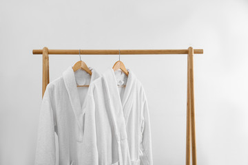 Fresh bathrobes hanging on rack near white wall