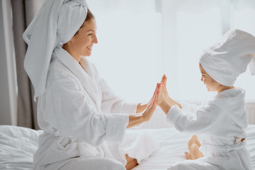 Obraz premium family game at home. friendly beautiful mother and her daughter sit clapping hands, play with each other, wearing white bathrobe and towel