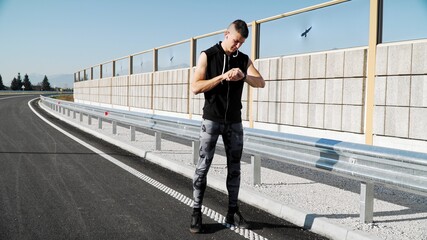 Young fit man jogging outdoors on the empty street and checking his smartwatch