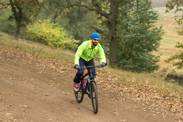 Cyclist in pants and fleece jacket on a modern carbon hardtail bike with an air suspension fork rides off-road.	