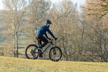 Naklejka premium Cyclist in pants and fleece jacket on a modern carbon hardtail bike with an air suspension fork rides off-road. 
