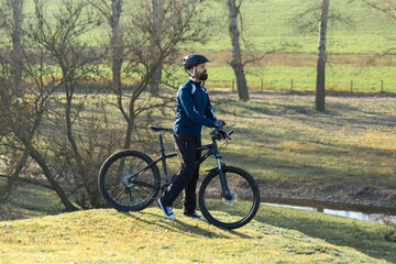 Cyclist in pants and fleece jacket on a modern carbon hardtail bike with an air suspension fork rides off-road.	