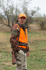 Hunting period, autumn season open. A hunter with a gun in his hands in hunting clothes in the autumn forest in search of a trophy. A man stands with weapons and hunting dogs tracking down the game.	