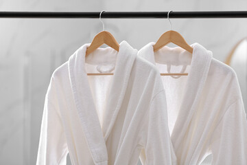 Fresh white bathrobes hanging on rack indoors - obrazy, fototapety, plakaty
