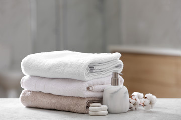 Fototapeta na wymiar Clean towels, spa stones and soap dispenser on table in bathroom