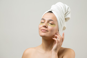 Young beautiful girl in a white towel on his head wears collagen gel patches under her eyes. Mask under eyes treatment face.	