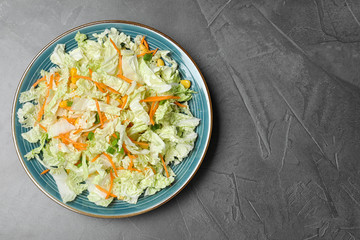 Plate of fresh cabbage salad with carrot on grey table, top view. Space for text