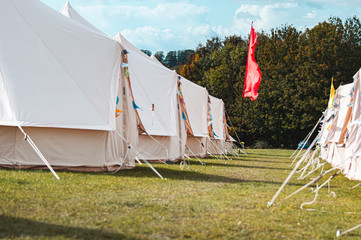 Light creme canvas waterproof tent in a green field on a nice and hot summer day. Blue Clouds, green grass, Child festival tent.